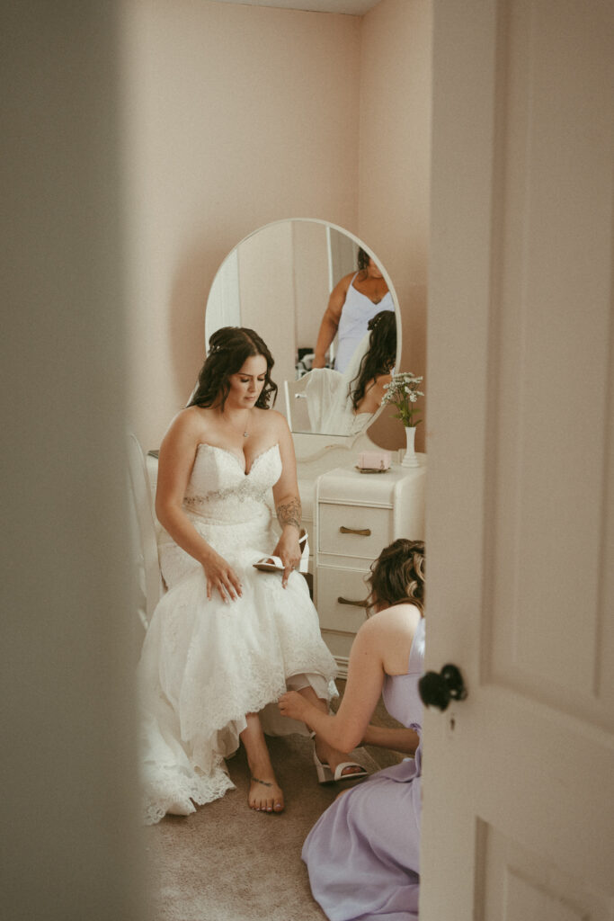 bride putting shoes on with bridesmaid's help