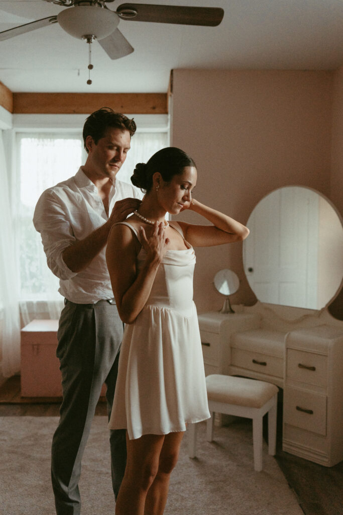 groom helping bride put on necklace after outfit change